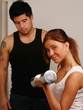 Girl lifting weight in gym, man in background