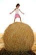 Girl playing over the round wheat dried bale Girl playing over the round wheat dried bale