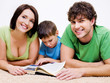 preschool boy reading book with his  parents
