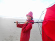 Foto: Cute teenage girl in a red raincoat with an umbrella at the beac Cute teenage girl in a red raincoat with an umbrella at the beac