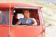 Handsome young guy driving a mini van on the beach