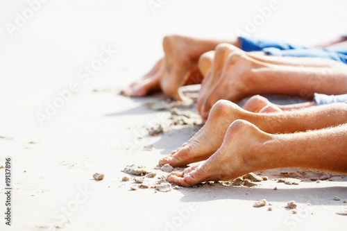 Foto: Group of a people relaxing on the beach, focus on their legs Group of a people relaxing on the beach, focus on their legs