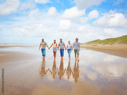 Happy young friends holding hands and walking on the beach