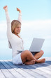 Happy young female with hands raised using on a laptop outdoors