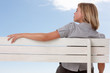 Female sitting isolated on a bench , sky at the back