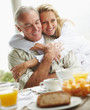 Romantic mature woman embracing her husband at breakfast table