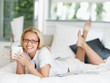 Smiling mature woman having coffee lying in bed