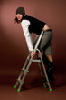 young tall girl in cap climbing on high ladder isolated