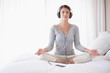 Woman with headphones in lotus position on bed by copyspace