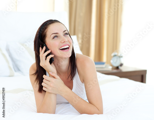 Foto: Radiant woman on phone lying on her bed Radiant woman on phone lying on her bed