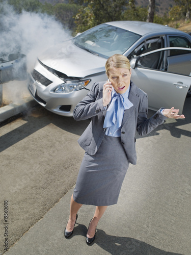 Photo: Businesswoman using cell phone near car wrecked on guardrail Businesswoman using cell phone near car wrecked on guardrail