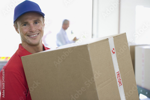 Photo: Delivery man holding cardboard box in warehouse Delivery man holding cardboard box in warehouse