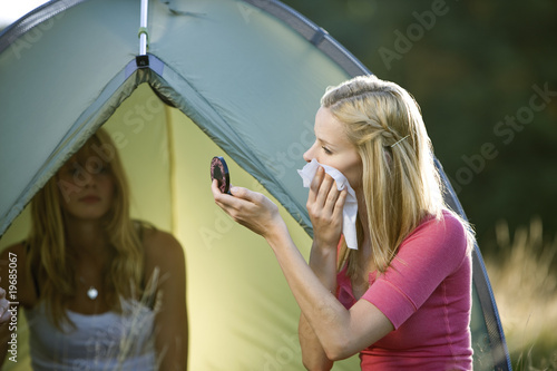 Photo: Two young women camping, one wiping her face Two young women camping, one wiping her face