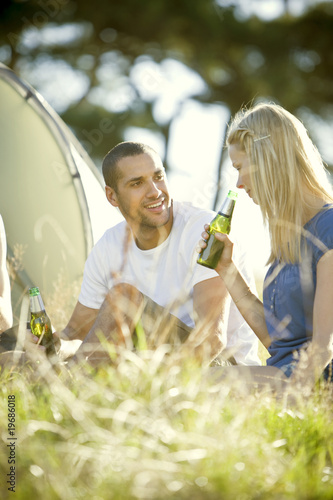 Photo: A young couple sitting in front of a tent, drinking beer A young couple sitting in front of a tent, drinking beer