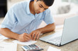 Young guy calculating his finances using calculator and laptop