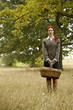 A young woman standing in a field, holding a wicker basket