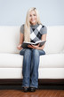 Young Woman Sitting on Sofa Holding Open Book
