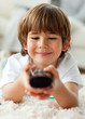 Cute little boy holding a remote lying on the floor