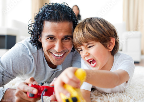 Photo: Excited little boy and his father playing video games lying on t Excited little boy and his father playing video games lying on t