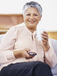 Senior woman holding TV remote while drinking coffee