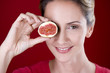 A mid adult woman holding half a fig in front of her eye
