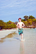 boy with red hair in swimsuit is running along the beach