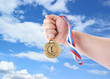 Hand holding gold medal on sky background