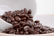 Whole dark roasted coffee beans spilling out of a cup Whole dark roasted coffee beans spilling out of a cup