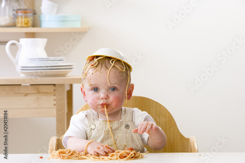 Photo: Messy baby boy in high chair with bowl of spaghetti on head Messy baby boy in high chair with bowl of spaghetti on head