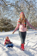 Mother Pulling Daughter On Sledge Through Snowy Landscape