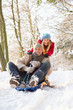 Couple Sledging Through Snowy Woodland