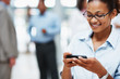 A happy female reading SMS with colleagues in the back