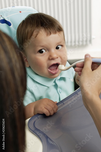 Foto: Young woman feeding baby boy in high chair Young woman feeding baby boy in high chair