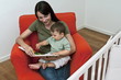 Young woman and baby boy sitting on arm chair reading a book