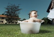 Baby boy taking bath in tub in garden and partial view of young woman with towel