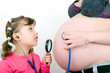Mädchen mit Stetoskop und Lupe vor Babybauch