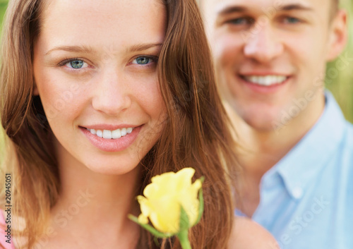 Foto: Beautiful young girl with flower and her boyfriend in background Beautiful young girl with flower and her boyfriend in background