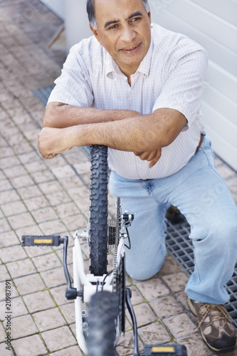 Photo: Mature man working on his cycle and lost in thought Mature man working on his cycle and lost in thought