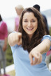 Smiling girl pointing at you with friends at the back