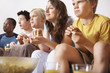 Teenagers watching television while eating popcorn