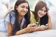 Young girls text messaging on cellphones while on couch