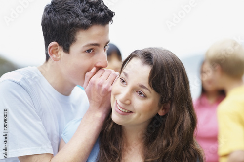 Photo: Young boy sharing a secret to a girl with friends in background Young boy sharing a secret to a girl with friends in background