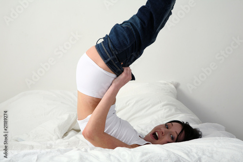 Foto: junge frau zieht ihre jeans im bett an junge frau zieht ihre jeans im bett an