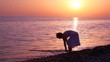 woman sloshing water in sea, sunset sky in background
