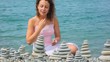 woman building stone stack on pebble beach, sea in background