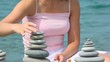 unidentified woman building stone stack on pebble beach