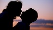 silhouettes of man and woman kissing, sunset sky in background