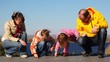 family sits and draws on asphalt against kind of river and sky