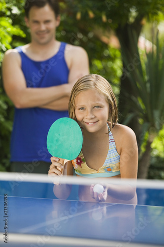Photo: girl (7-9) playing table tennis with father in background. girl (7-9) playing table tennis with father in background.