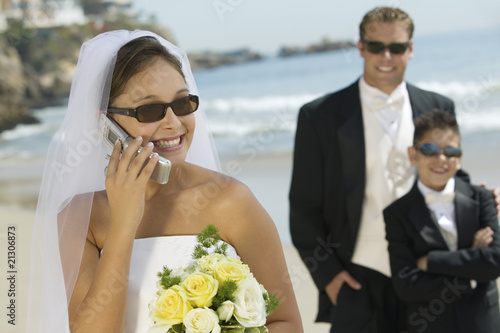 Photo: bride using mobile phone groom and brother in background bride using mobile phone groom and brother in background